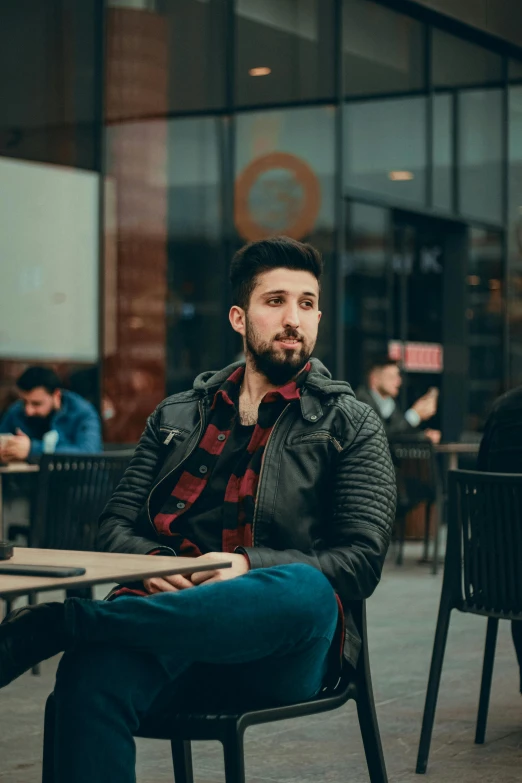 a man sitting at a table with a beard in a leather jacket