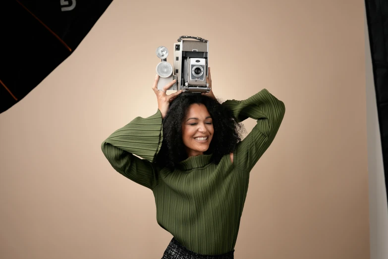 a black woman holds an old fashioned camera up in the air