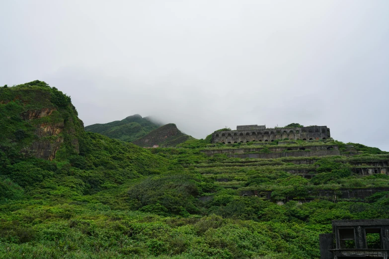 a stone building on a hill with trees and shrubs