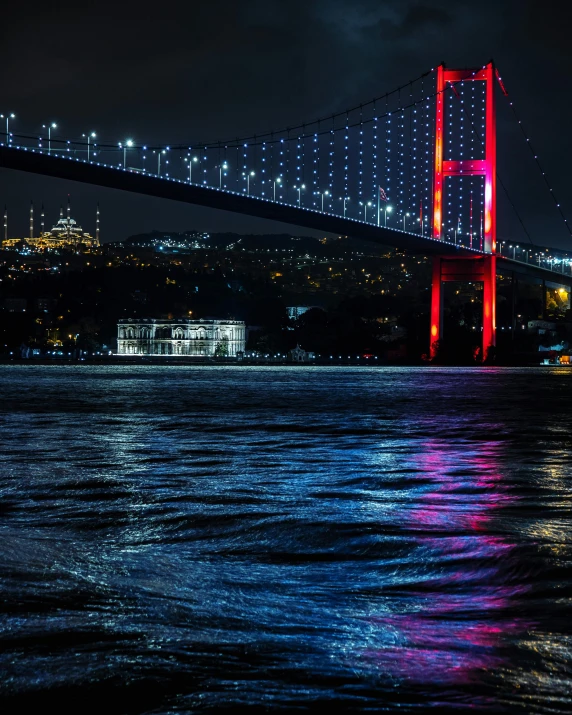 colorful lights are lit up on the bridge above the water