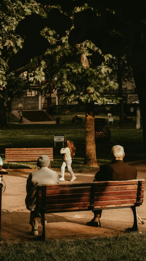 three people sit on a park bench next to trees