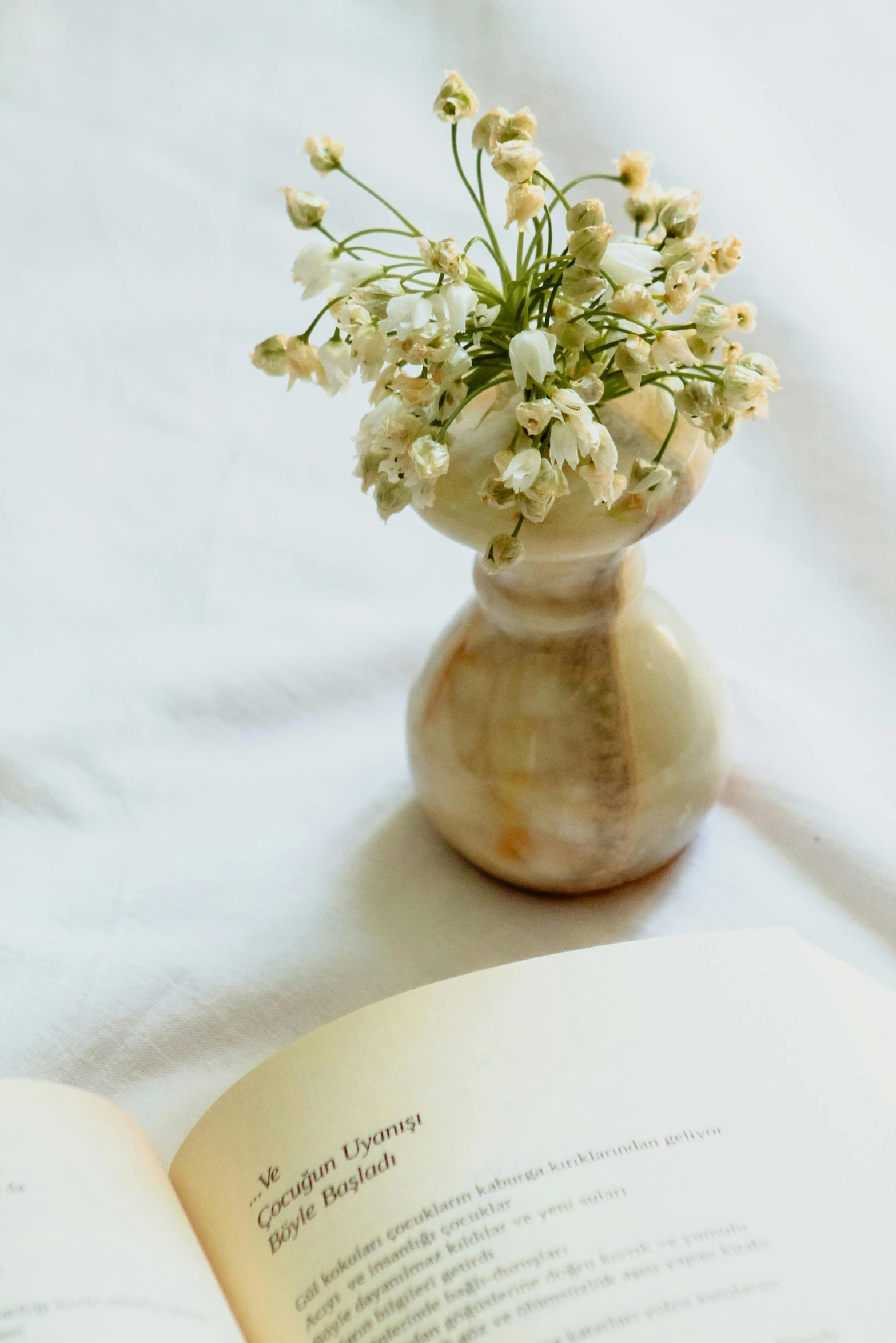 a white book on a table next to a vase filled with white flowers