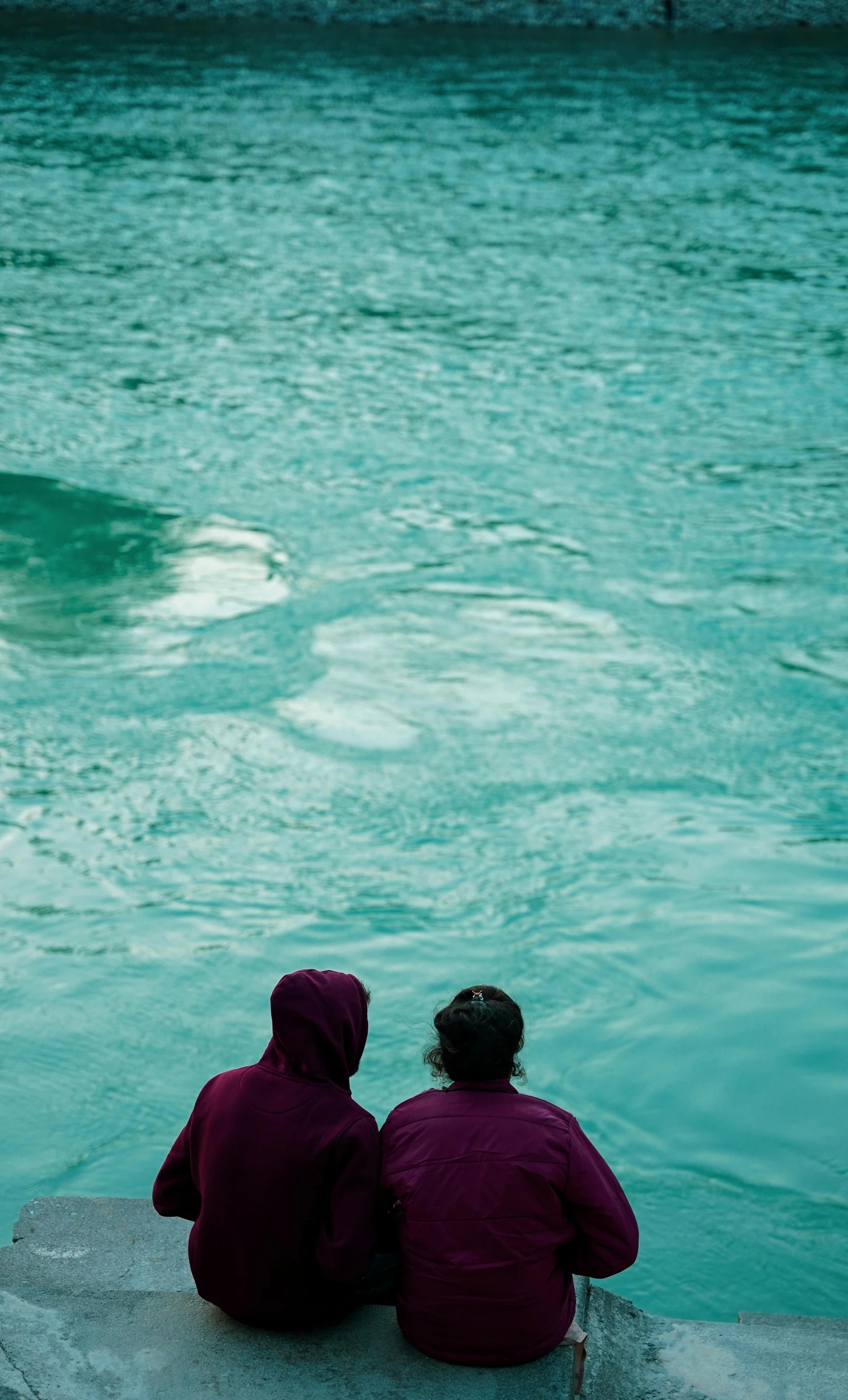 two people sitting on rocks near the water