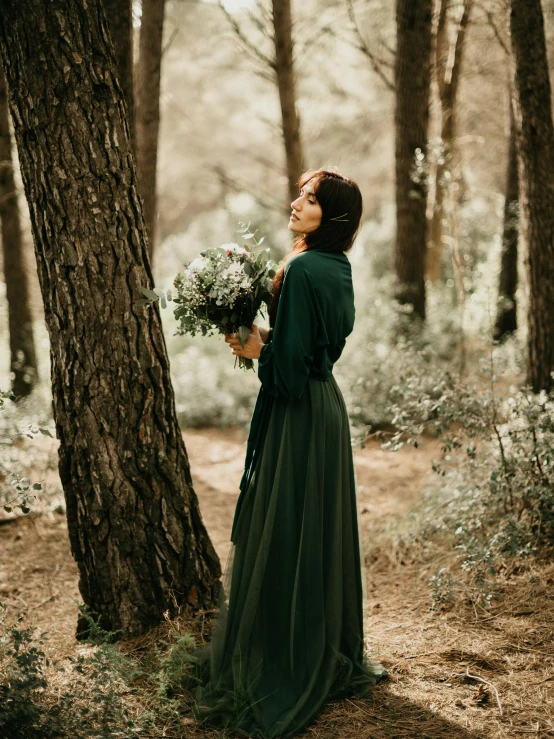 woman in long dress standing next to tree in woods