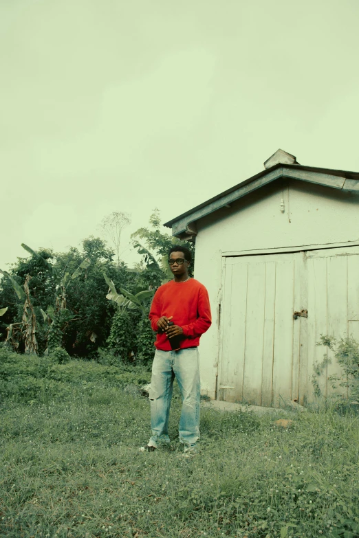 a man in red standing in the grass near a building