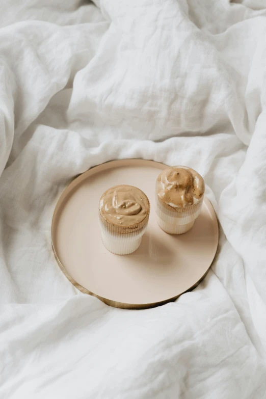 two cupcakes sit on a plate and cover a bed
