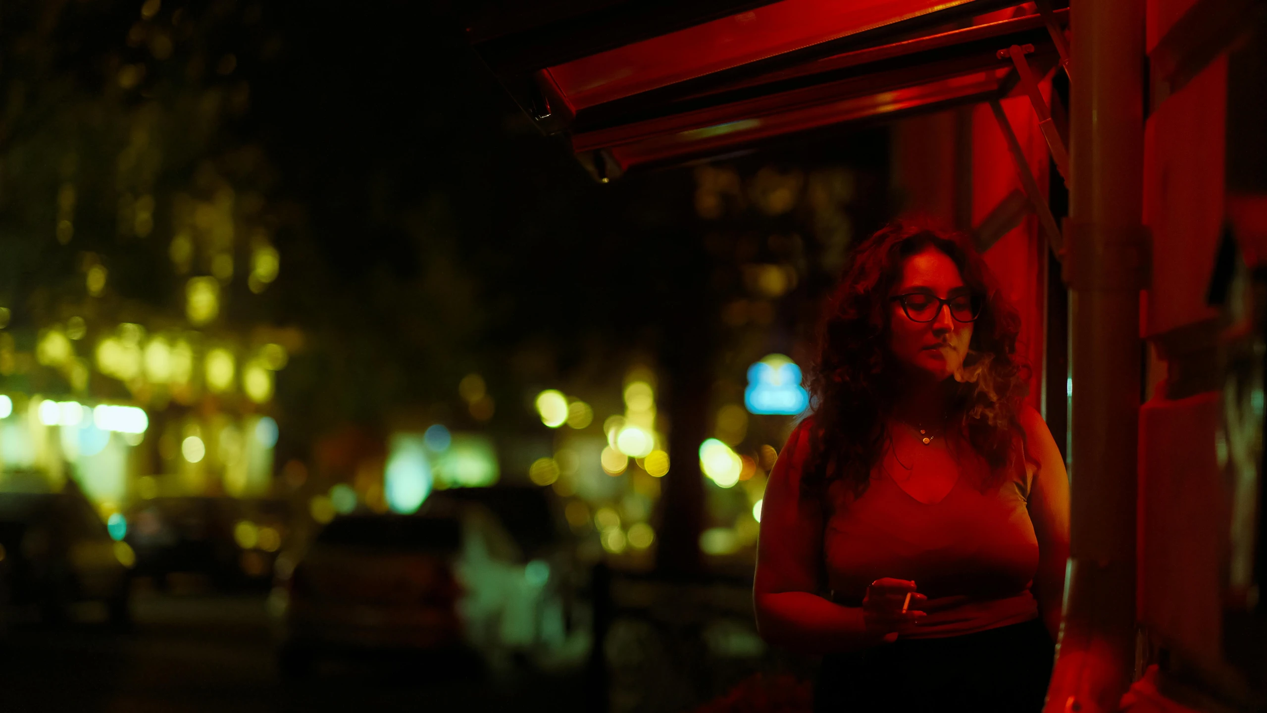 a woman stands under a red lit awning