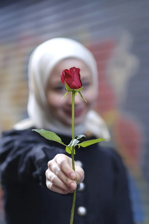 a person with a black jacket and a white head scarf holding a rose