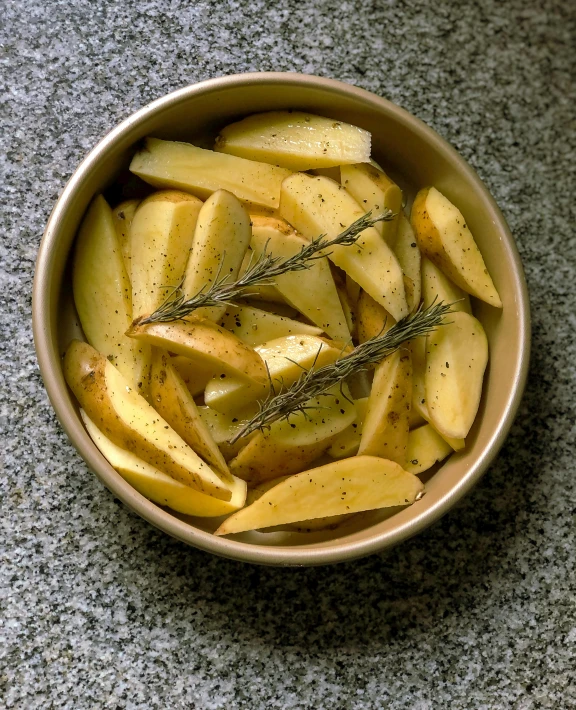 a bowl with seasoned sliced potatoes in it