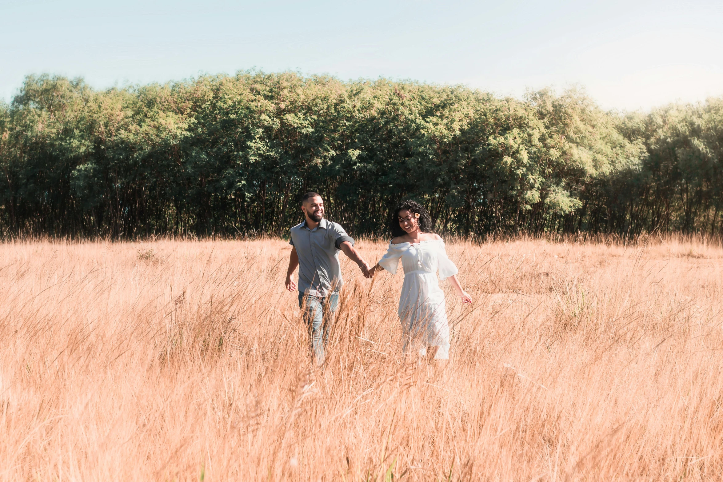 the young couple is holding hands walking in the long grass