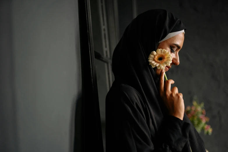 a young woman wearing a hijab holds a flower in her hand