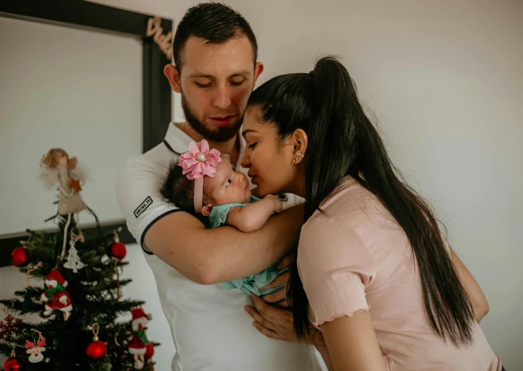 two adults hug a baby on the forehead