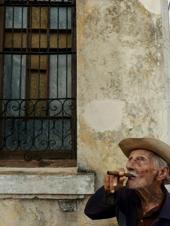 a man in a straw hat sitting outside a building while smoking