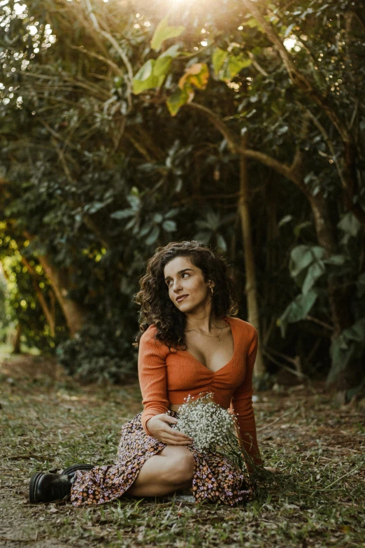 a woman in an orange top sitting in the middle of the grass