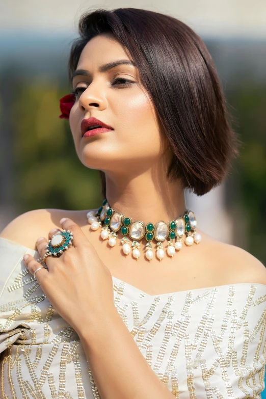 a woman wearing a white dress holding onto her emerald and pearl necklace