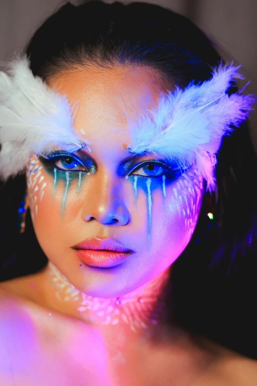 a woman wearing white and blue makeup with feathers on her head