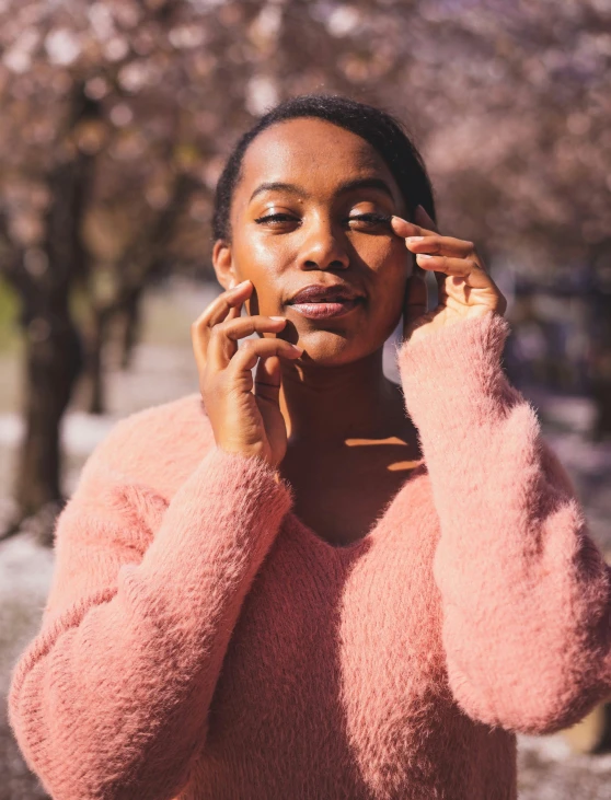 an african american woman in a pink sweater holds her ear in front of her head