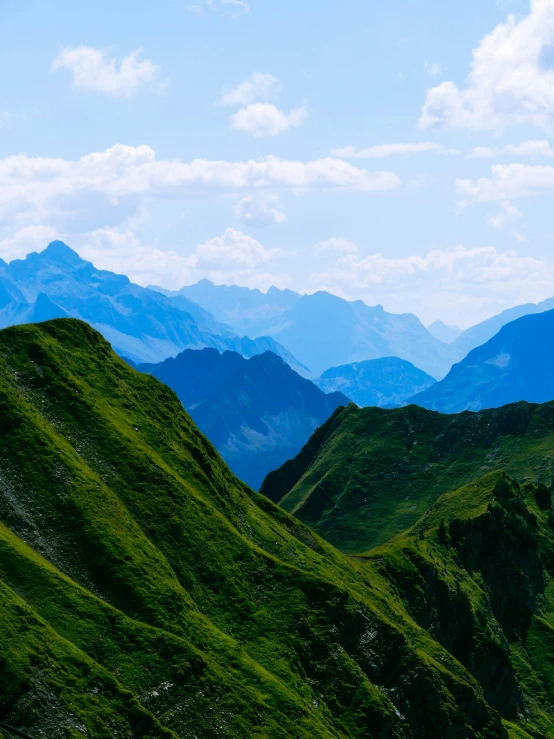 the grassy hills are green and with the mountains behind it