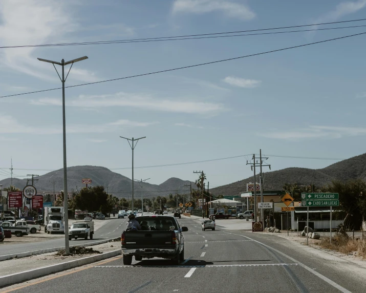 a road that has cars on it, parked on both sides and mountains behind