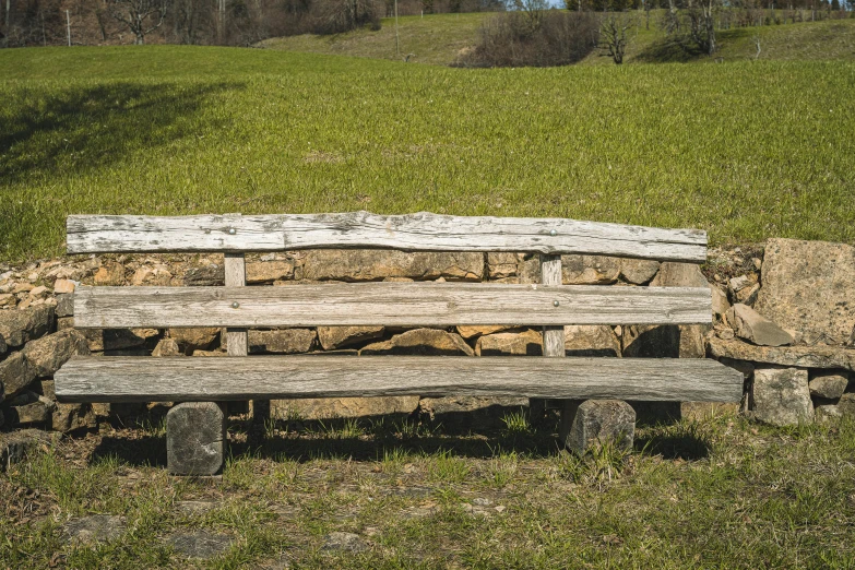 this is a rustic bench in the grass near rocks