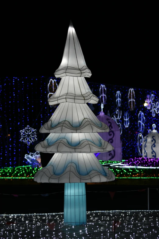 a lighted tree sits atop a platform in front of several buildings with white lights