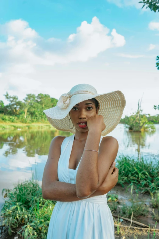 a woman wearing a large hat stands by the water