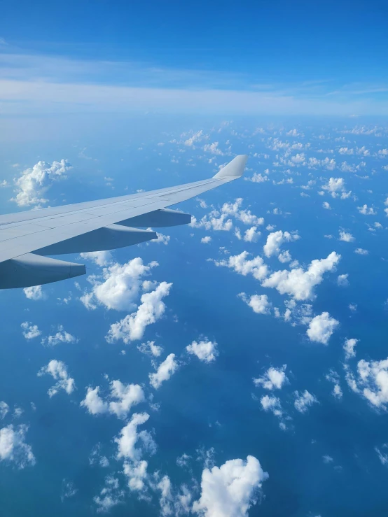 a plane wing in the sky with some clouds below