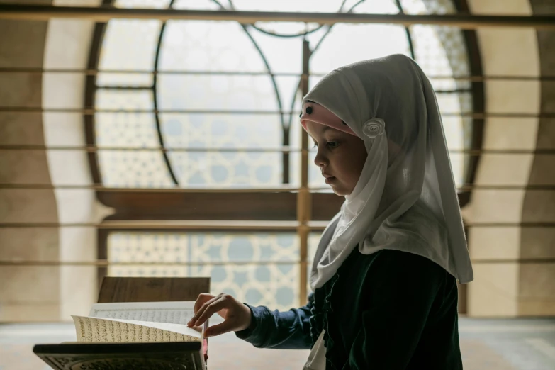 a nun reading a book next to a large stained window