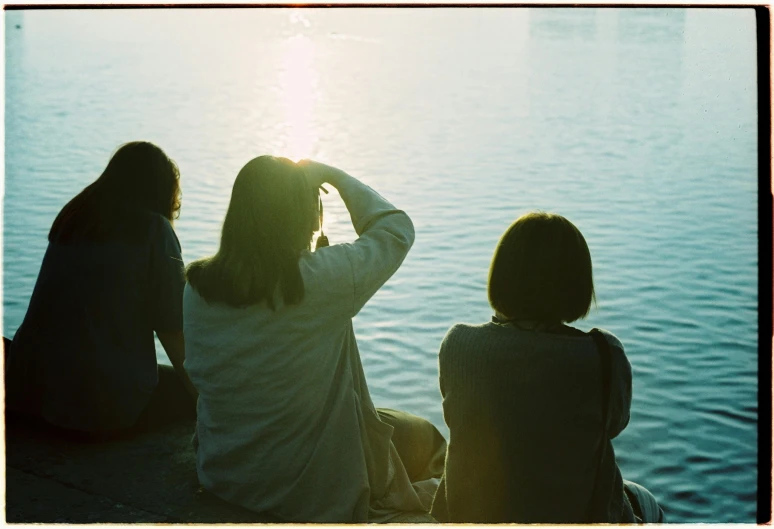 three women sitting by the ocean with their arms on their forehead