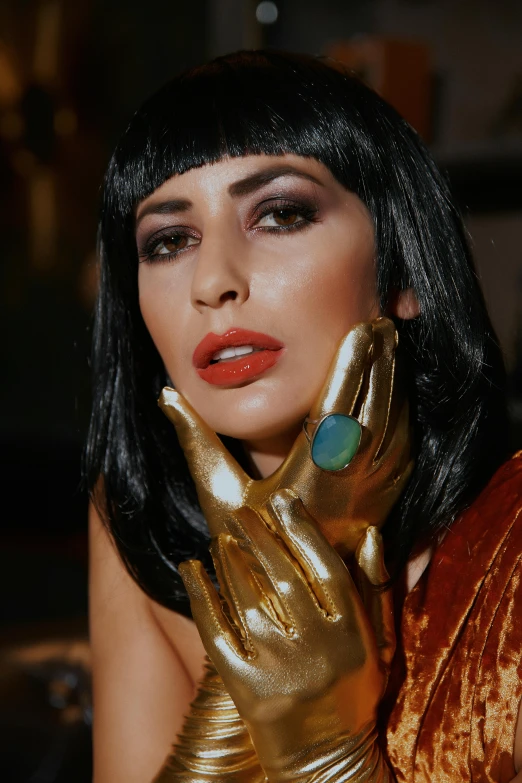 a woman in gold latex poses with her hand on her face