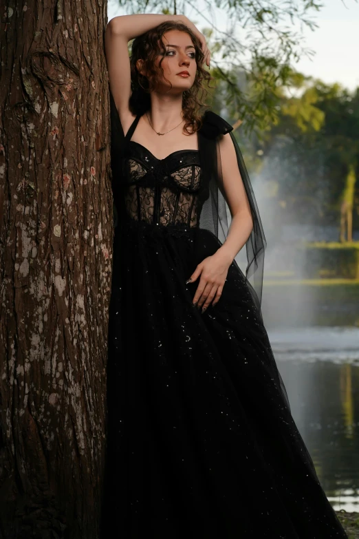 a woman in a black dress leans against a tree