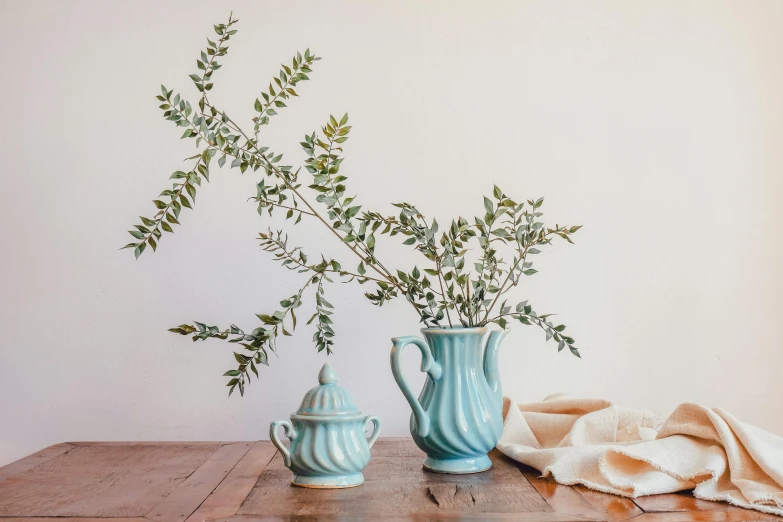 two vases with different green plant stems sit on a wood table