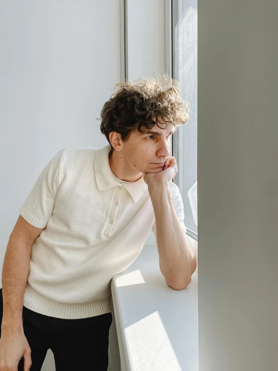 a man leans against a wall and looks at the window