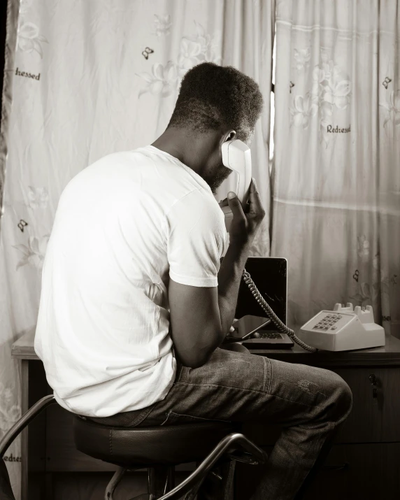 black and white image of man sitting in chair on phone