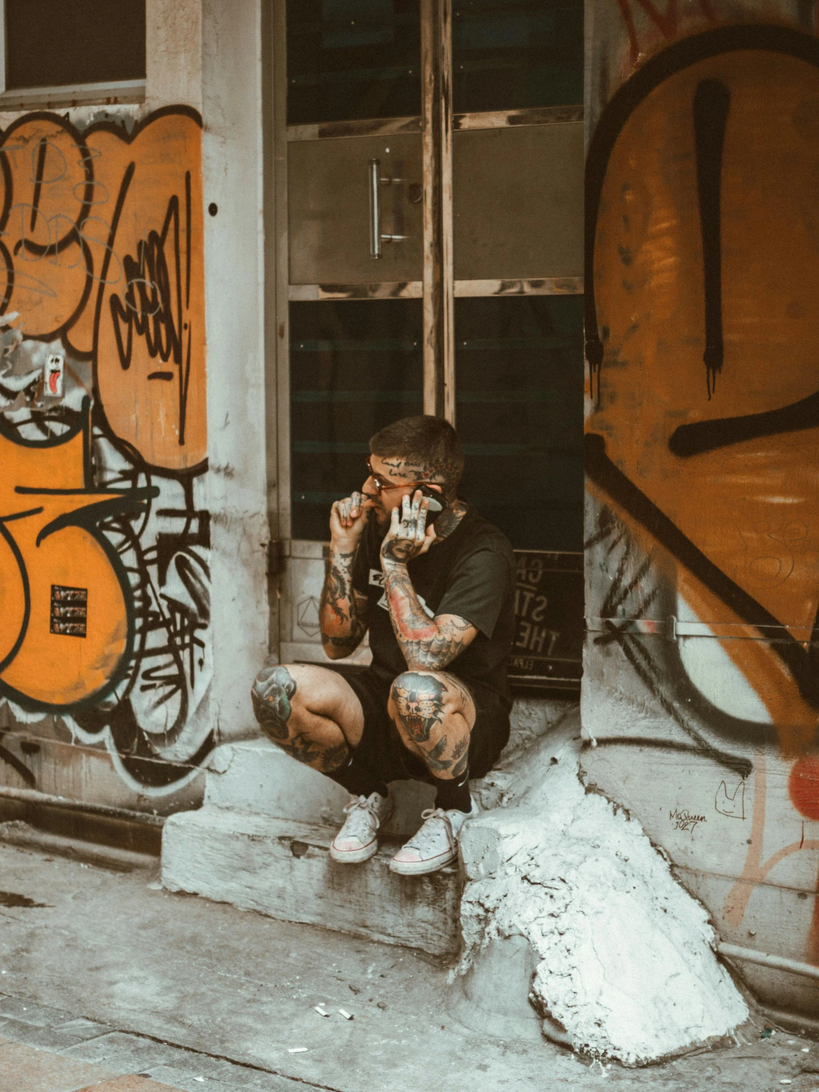 man in black shirt and white shoes sitting on steps next to graffiti