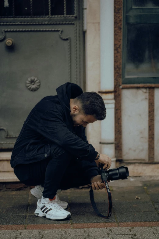 a young man sits on a curb with a pair of tennis shoes while holding a camera