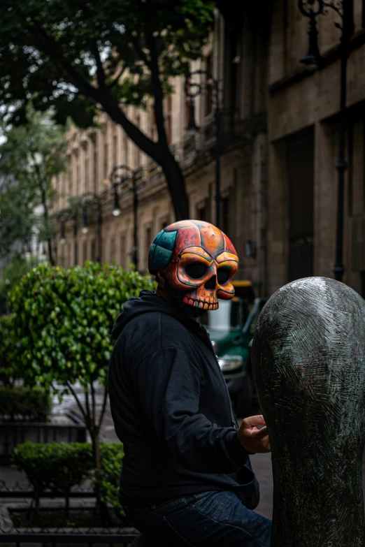 man sitting on park bench wearing colorful skull headgear