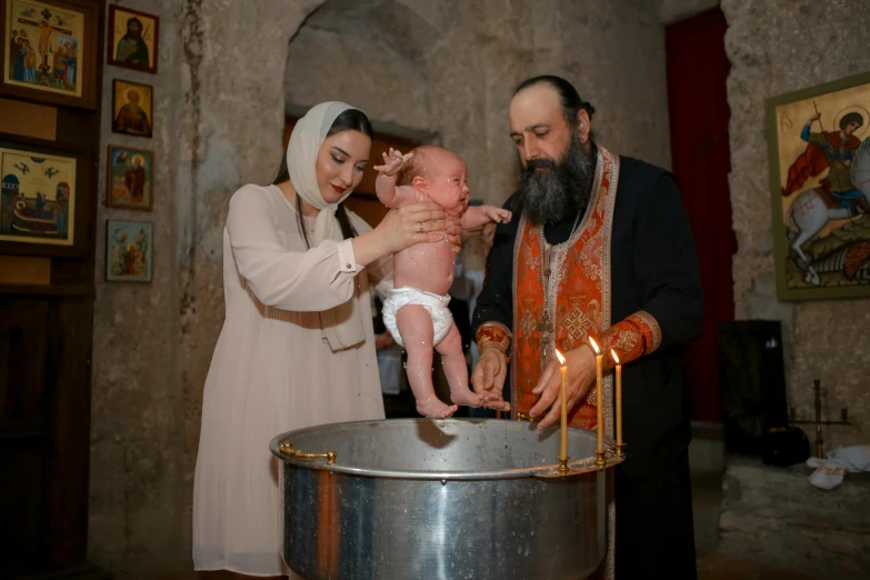 a man and woman dressed in a religious wedding outfit are holding a baby and feeding them cake