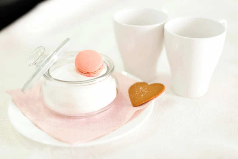 two cup on a pink towel with a heart shaped cookie and an empty glass jar