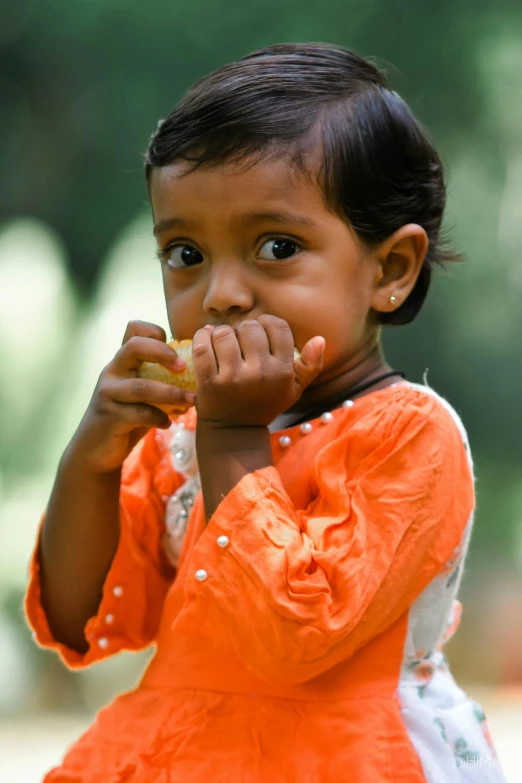 a child wearing an orange dress eating soing