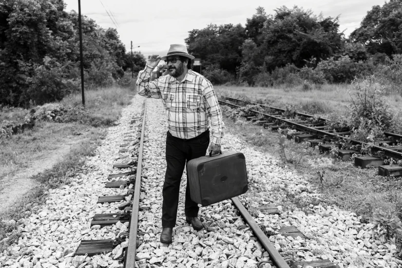 a man stands near train tracks holding a suitcase
