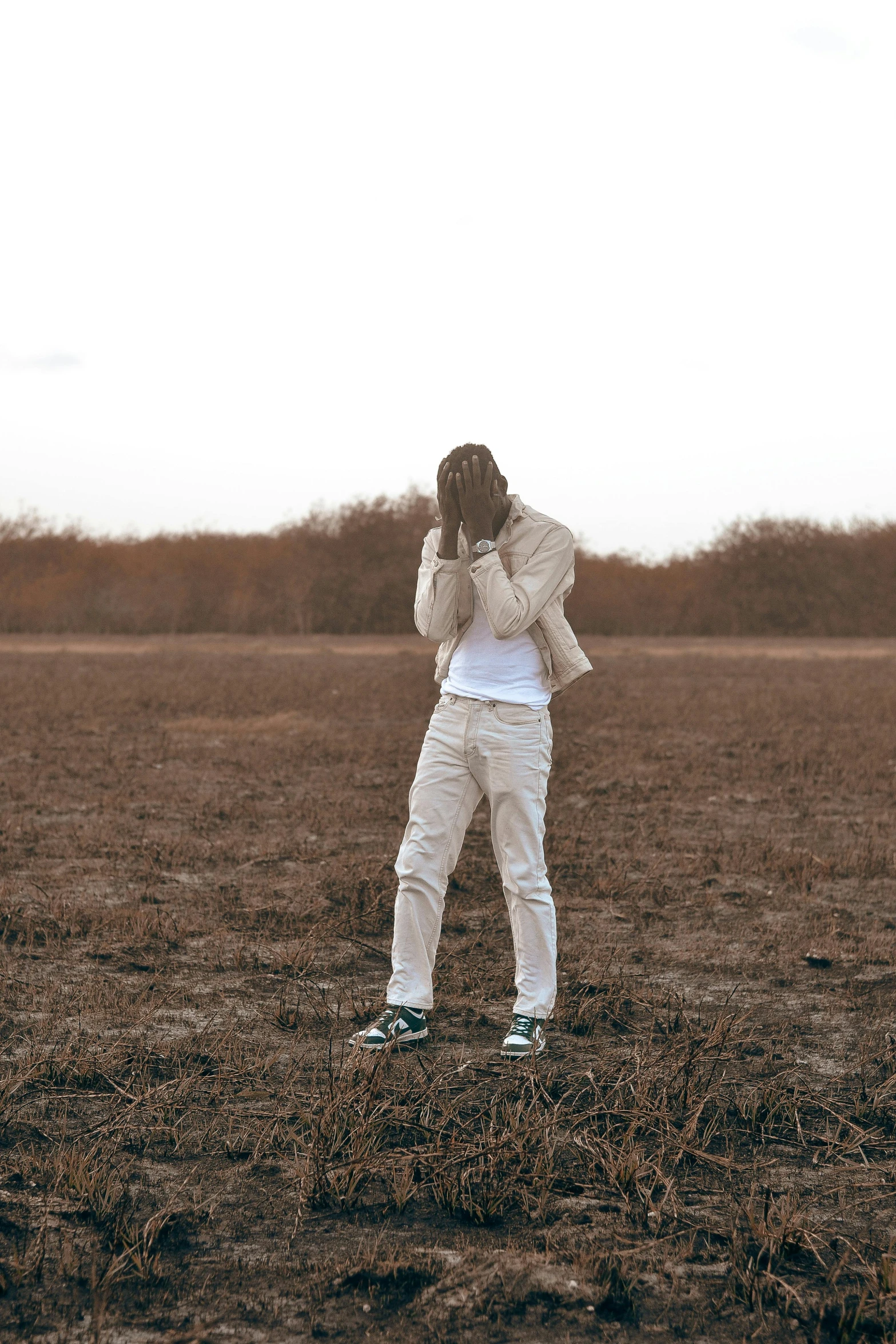 a person wearing white pants stands on a field and covers his face