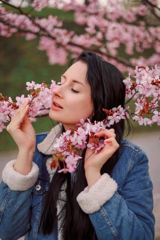 a girl with black hair and a denim jacket holding some flowers in her hands