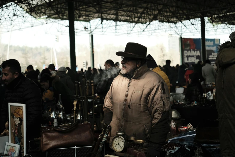 a man wearing a rain coat and hat holding a clock in his hands