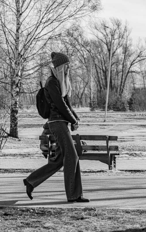 black and white image of man in denim pants walking with handbag and hat