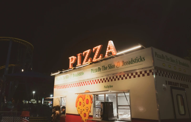 a person outside of a large pizza stand at night