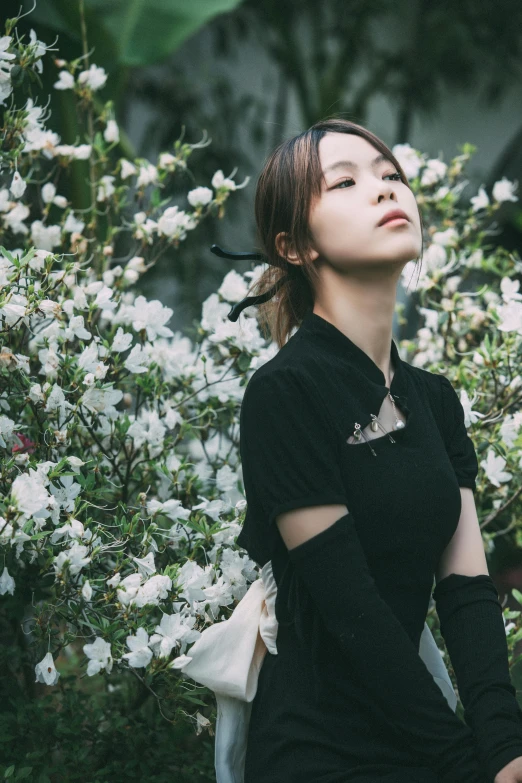 an asian woman in black standing near flowers