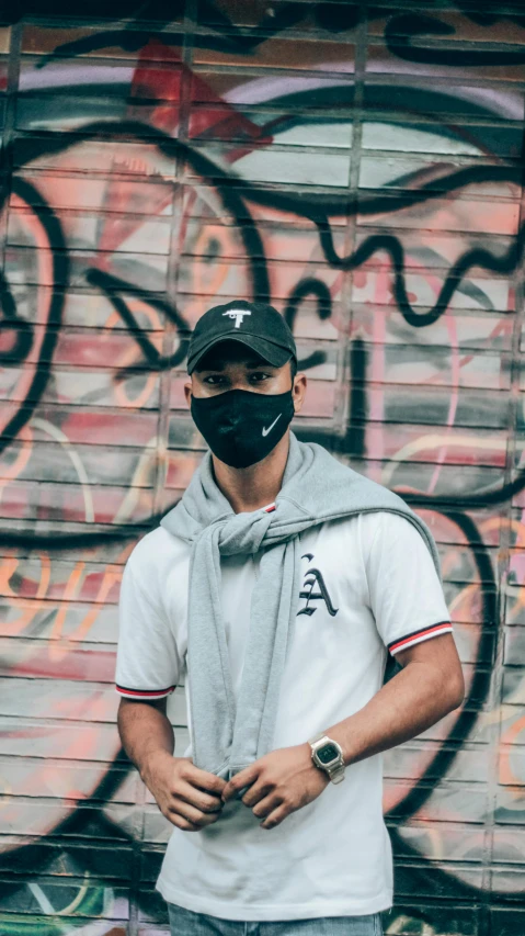 man wearing face mask, with hoodie, standing in front of wall with graffitti