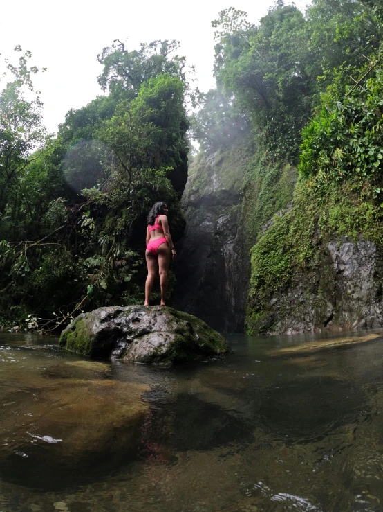 woman in pink bathing suit standing on rock next to water