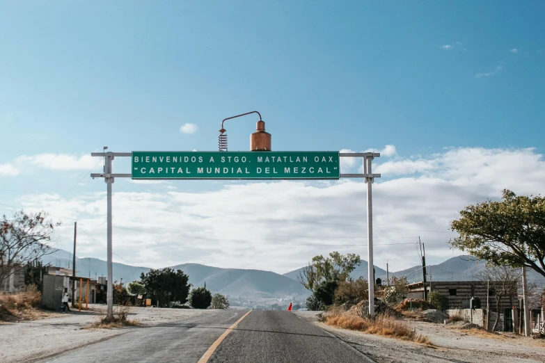 a large sign over an empty road in a rural area